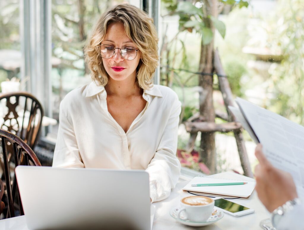 Professional woman working on a laptop in a modern cafe setting, ideal for illustrating the comparison between MacBook vs Windows laptops 2025 in a corporate productivity context.
