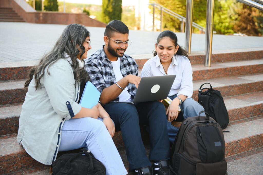 Three college students happily studying outdoors using a laptop, symbolizing collaboration and efficiency, ideal for showcasing affordable laptops for college students.