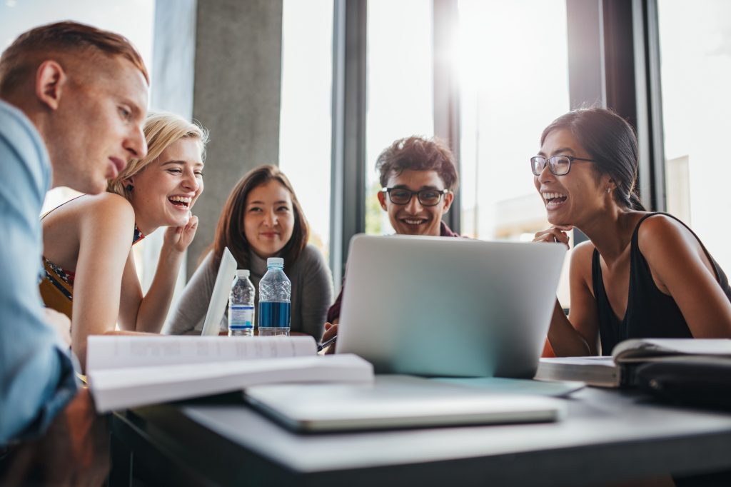 A group of cheerful university students collaborating around a laptop, representing teamwork and productivity, ideal for reviewing top student laptops 2025.