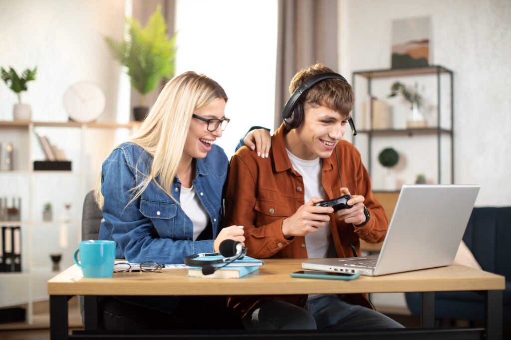 Young gamers enjoying a laptop gaming session together, highlighting performance and affordability of gaming laptops under 1200 dollars in a modern home setup.