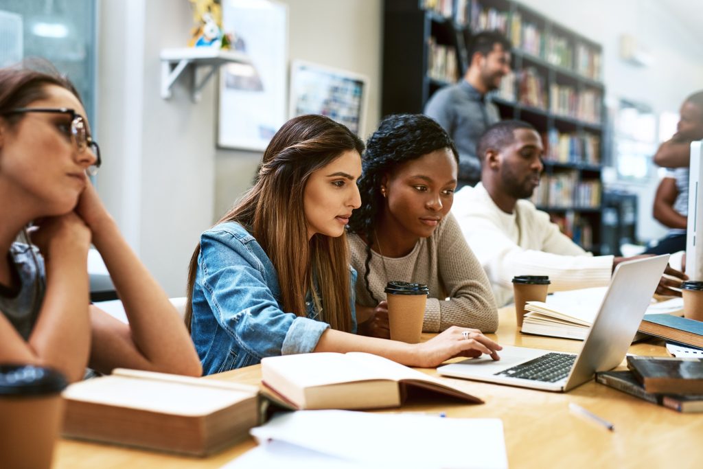 Group of diverse students studying together in a modern library using laptops, highlighting collaboration and productivity, ideal for showcasing the best laptops for students 2025.