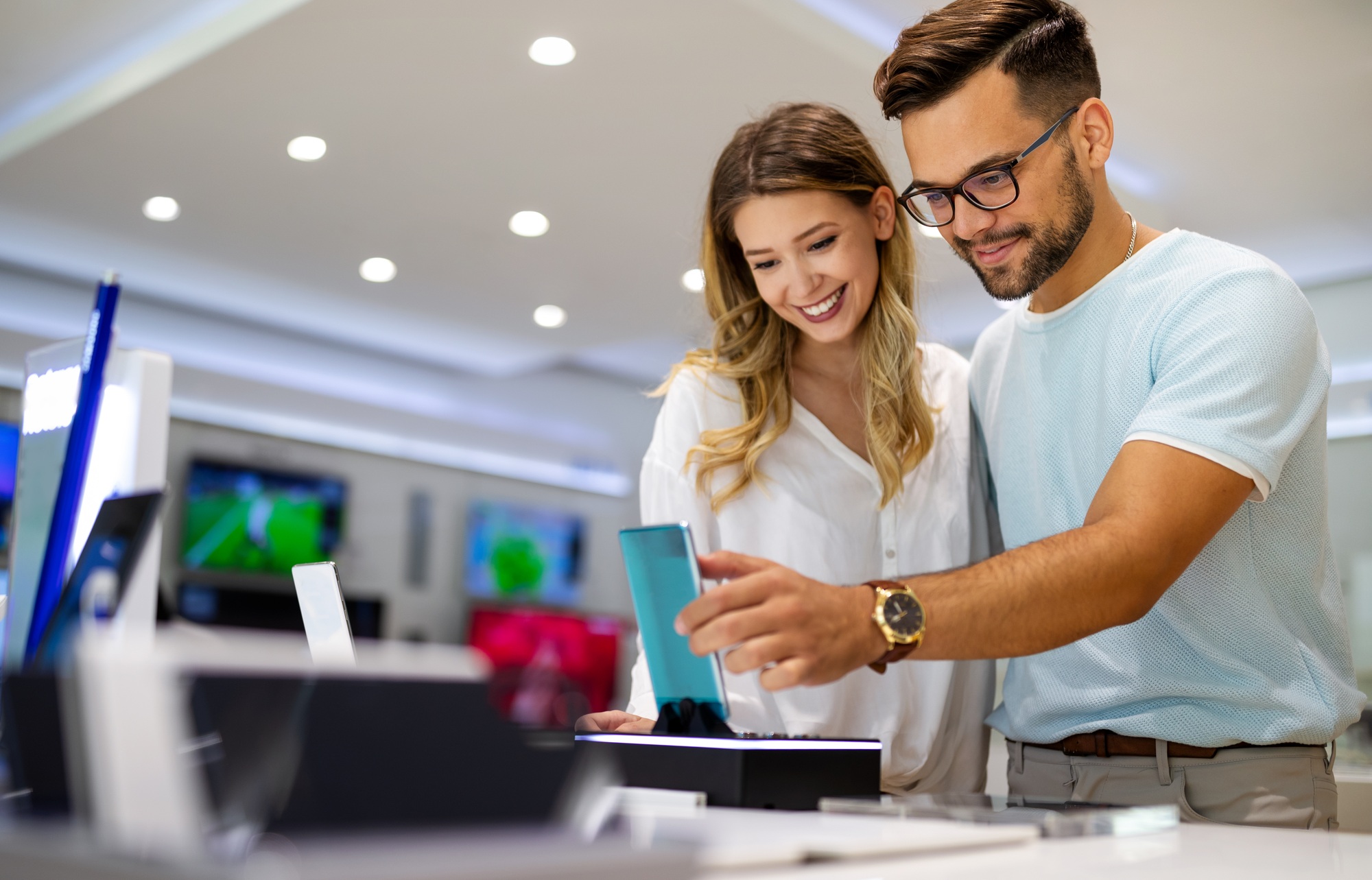 Smiling couple exploring smartphones at a tech store showcasing the latest UnitedTech Deals on electronics and gadgets.