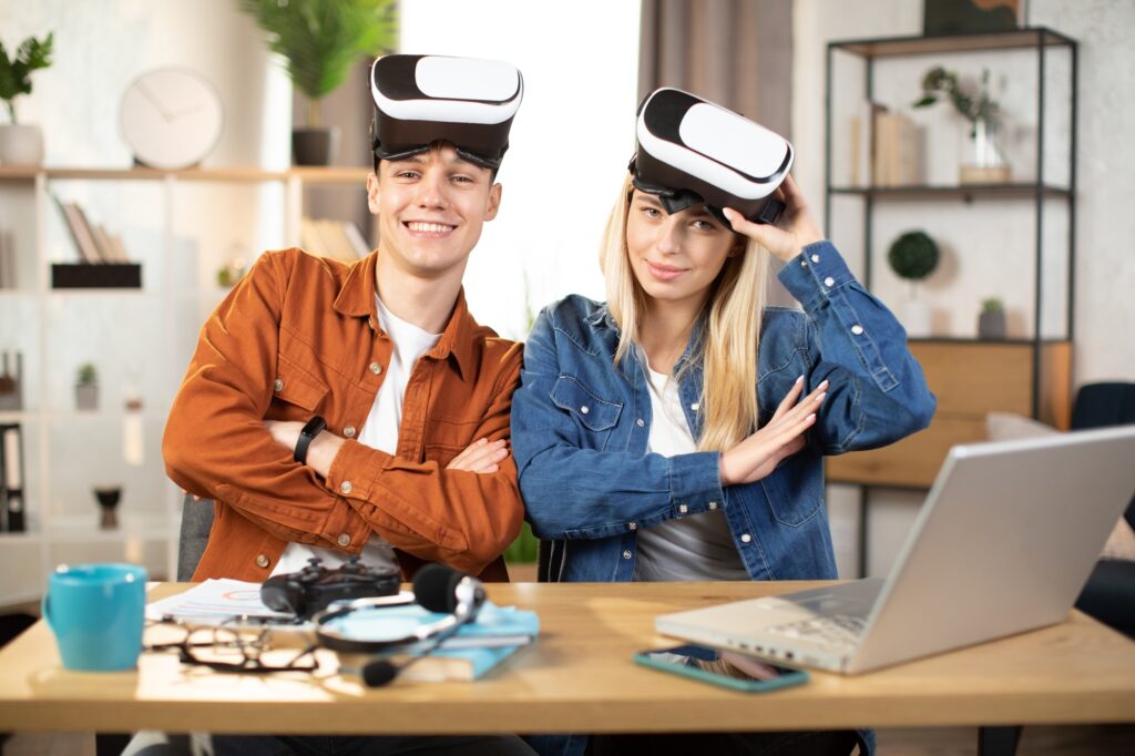 Two young gamers wearing VR headsets and smiling in a modern workspace, representing the excitement and performance offered by affordable gaming laptops.