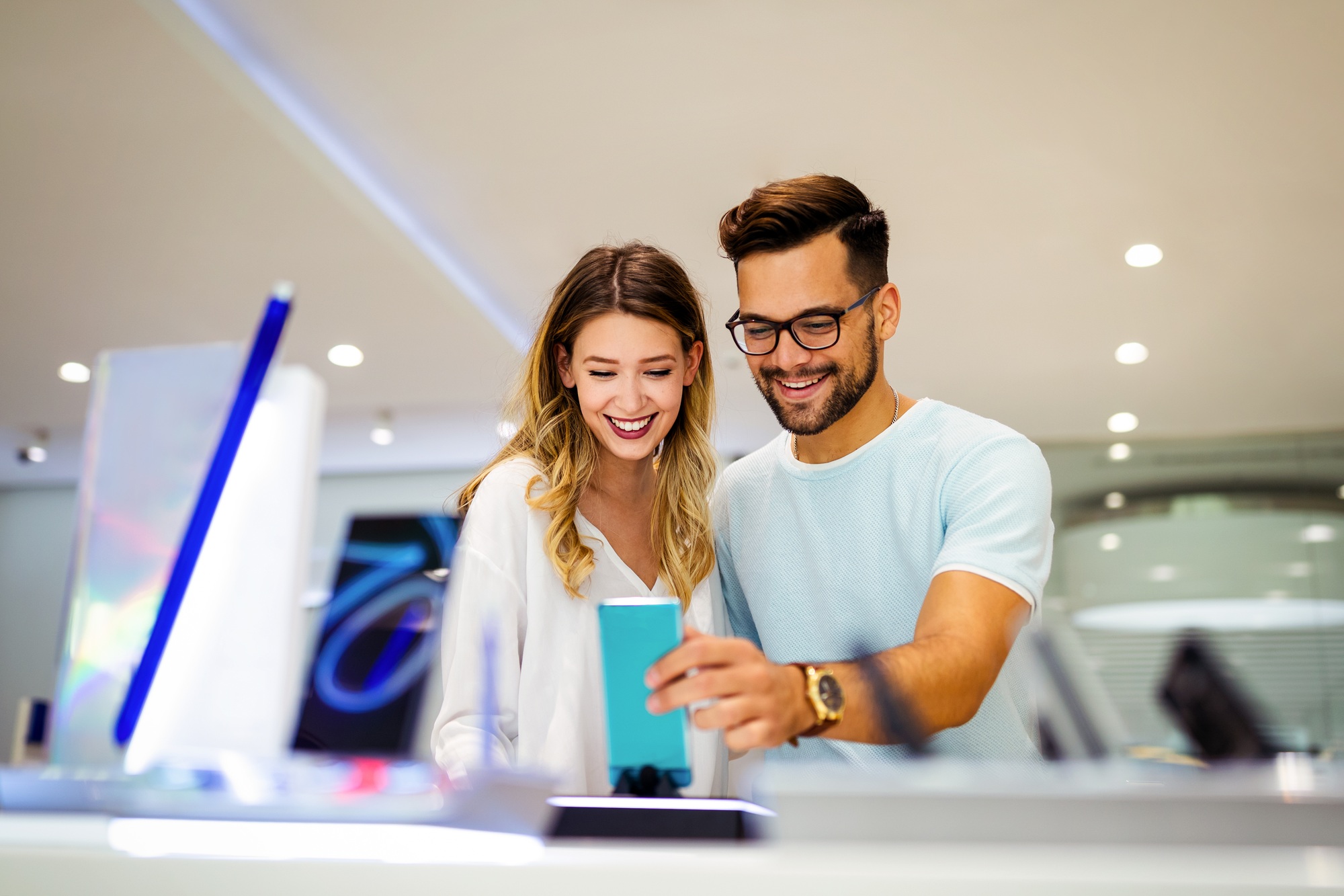 Smiling couple exploring the latest smartphones at a UnitedTech electronics store, showcasing premium devices and a modern shopping experience.