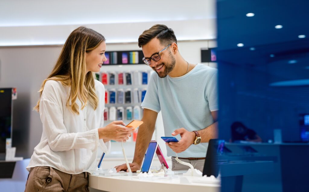 Customers exploring the latest smartphones in a tech retail store, showcasing product engagement and expert advice—ideal for illustrating consumer-focused insights on the UnitedTech Deals Blog.