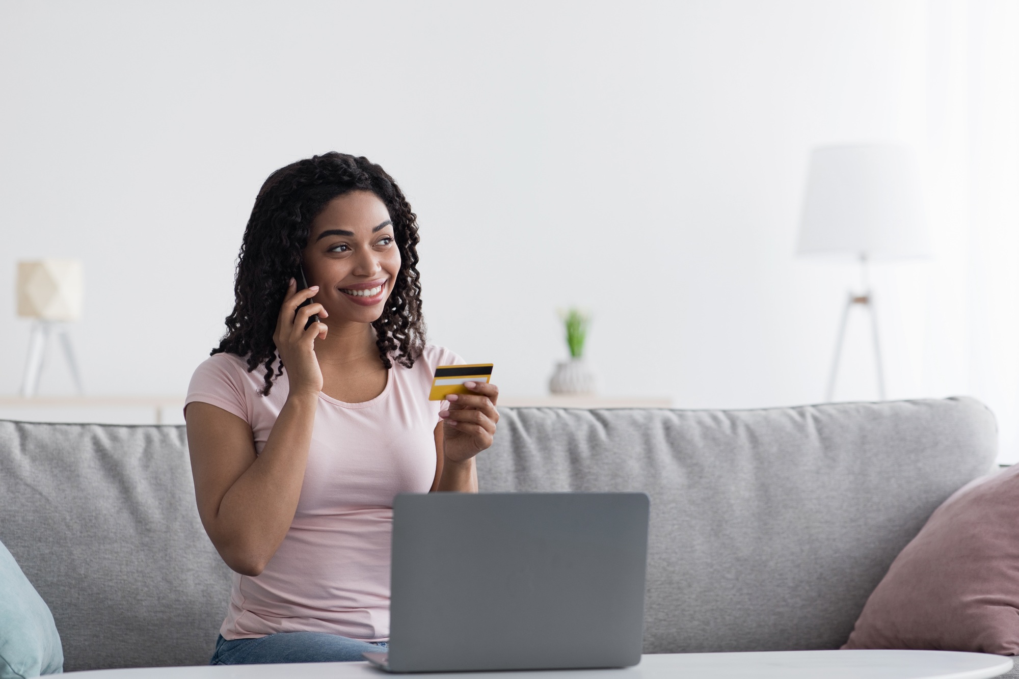 Happy customer sitting on a couch holding a credit card while calling UnitedTech Deals phone number for online purchase support, with a laptop open in front — ideal visual for customer service and eCommerce assistance.

