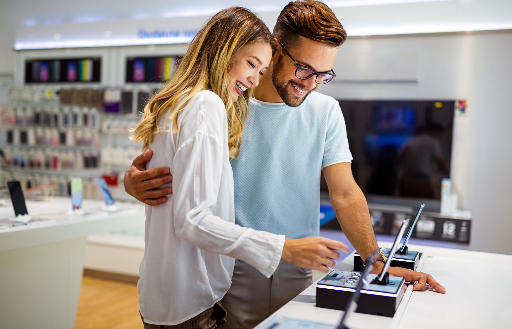 Happy couple exploring smartphones at a modern electronics outlet store, browsing the latest mobile deals and tech offers together.